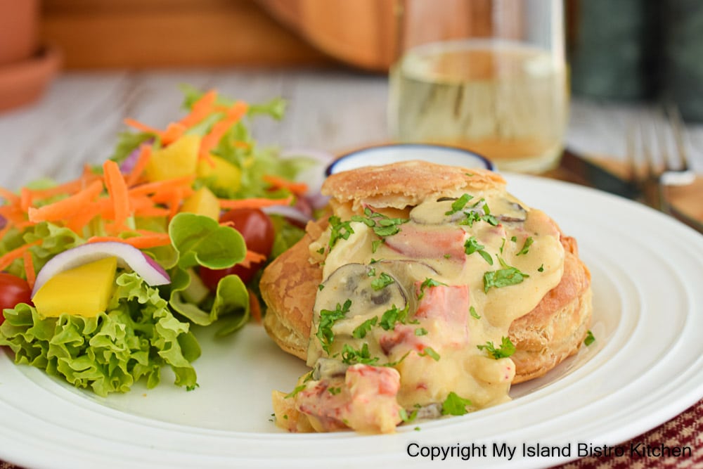 Plated meal of creamed lobster in a patty shell with a side green salad. A glass of white wine is in the background.