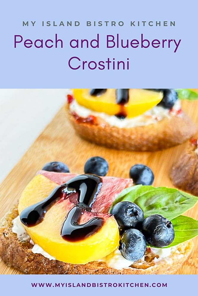 Blueberries, a peach wedge, cold cut, and basil leaves on a jelly and cream cheese topped baguette slice form a tasty crostini