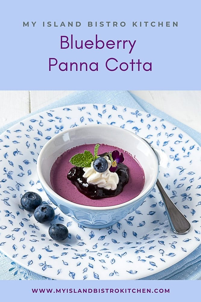 Panna Cotta topped with blueberry sauce and a dollop of whipped cream in blue bowl sits on pretty blue patterned plate