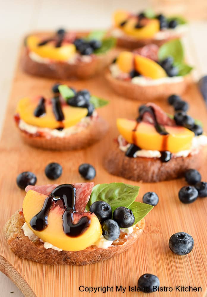 Serving board topped with crostini made made with peaches and blueberries