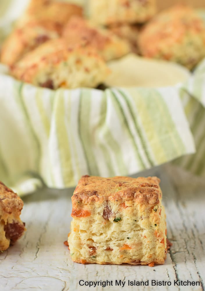 A savory scone sits outside a tea towel-lined basket full of scones on counter