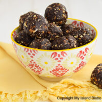 White, red, and yellow bowl filled with energy balls sits on a bright yellow fringed napkin