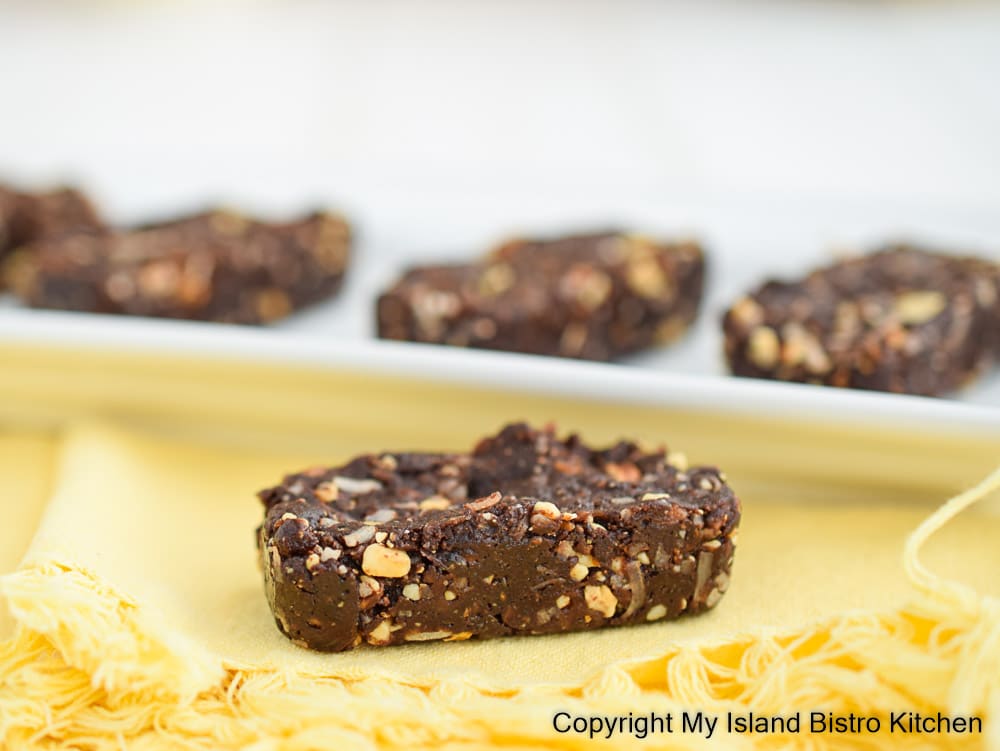 Close-up photo of a small rectangular energy bar sitting on a yellow fringed napkin with a white tray of more energy bars in background