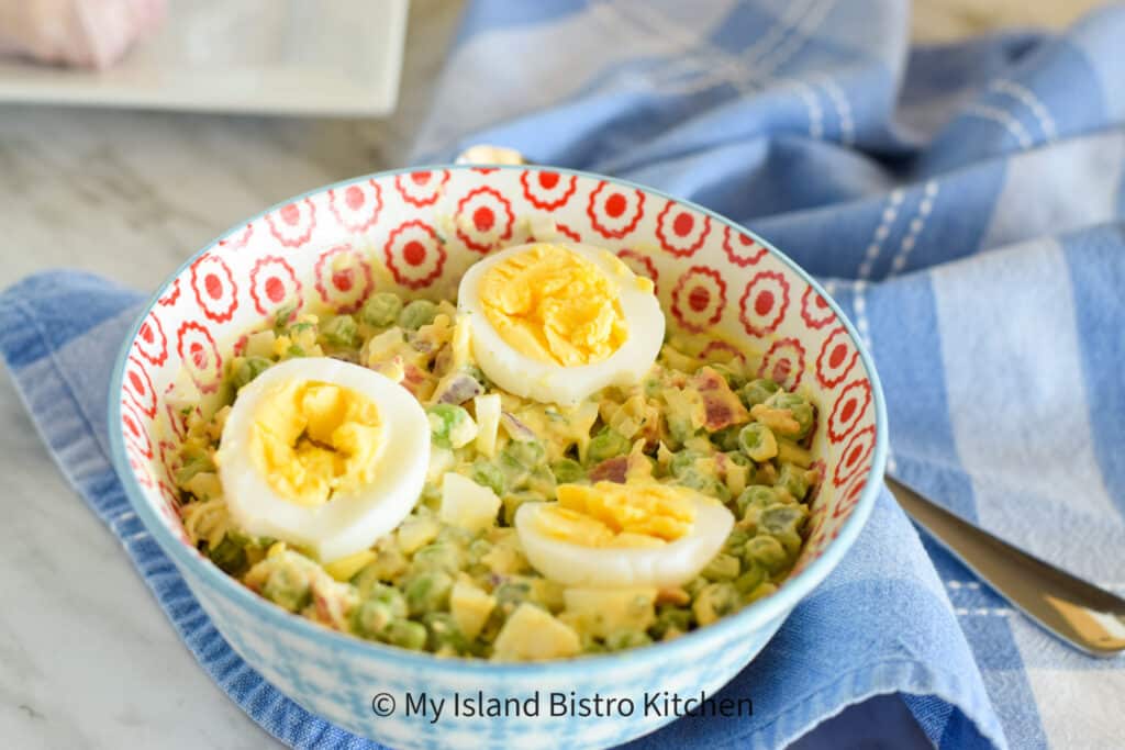 Bowl filled with salad made with fresh green peas, hard-boiled eggs, crispy bacon, red onion, celery, and shredded cheese