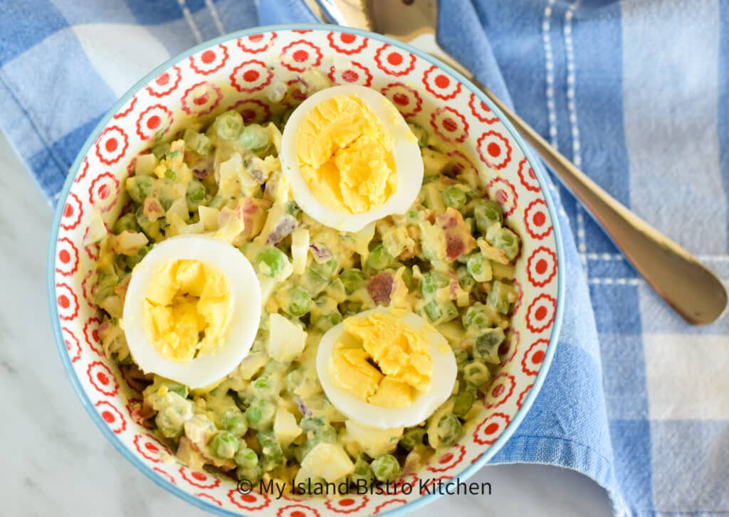 Bowl of salad made with fresh peas, hard-boiled eggs, crispy bacon, red onion celery, and cheese