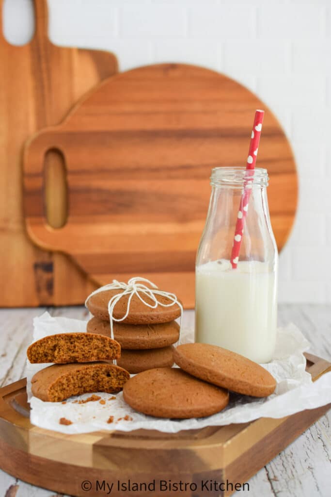 A board, topped with a stack of homemade cookies and bottle of milk, sits on counter with cutting boards in the background