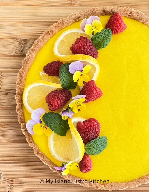 Lemon Tart is garnished with fresh fruit, lemon wheels, and edible flowers.