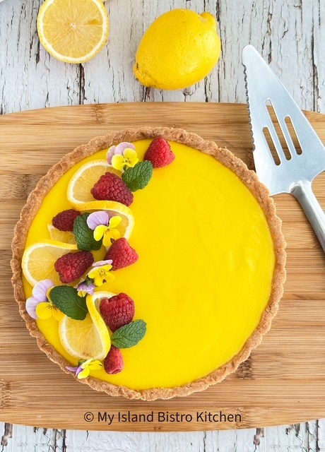 Overhead view of Lemon Tart garnished with raspberries, mint leaves, lemon wheels, and edible flowers.