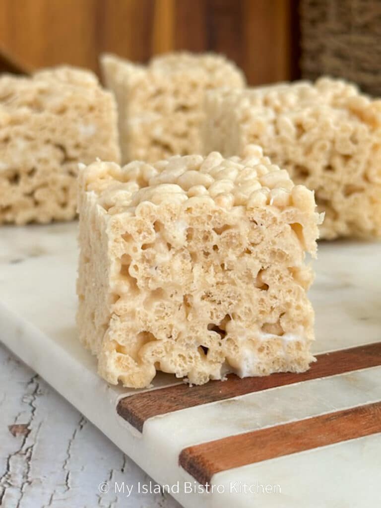 Close-up photo of old-fashioned Rice Krispies Squares sitting on a marble board on counter.