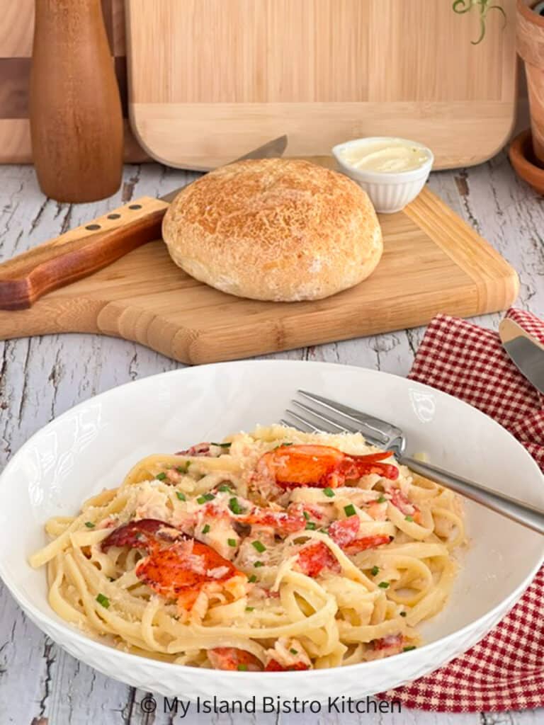 Bowl of lobster with pasta. Crusty bread on bread board in background