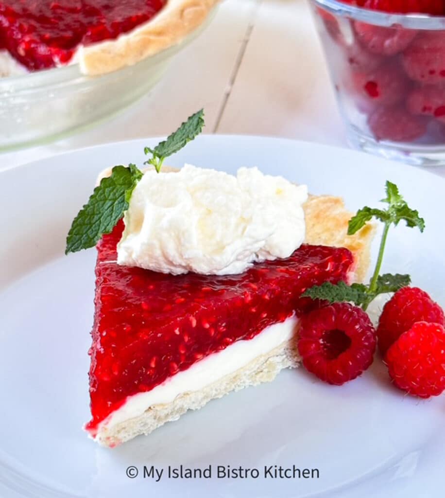 A showy slice of pie with cooked raspberry filling on top of a cream cheese layer and topped with whipped cream