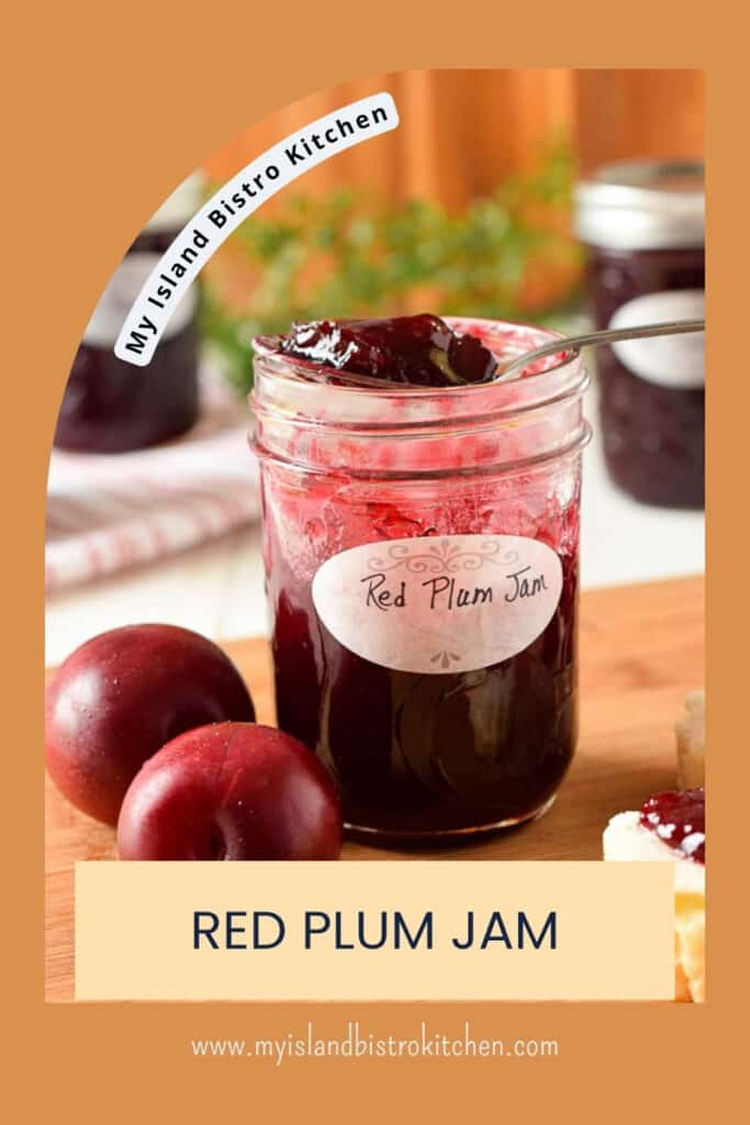 A spoonful of jam sits atop an open jam jar with red plums beside it.