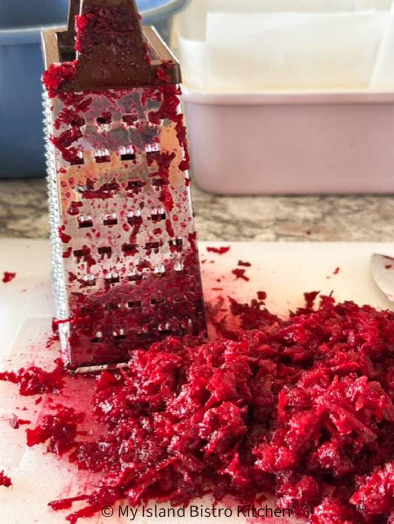 A box grater sits on cutting board along with grated raw beet.