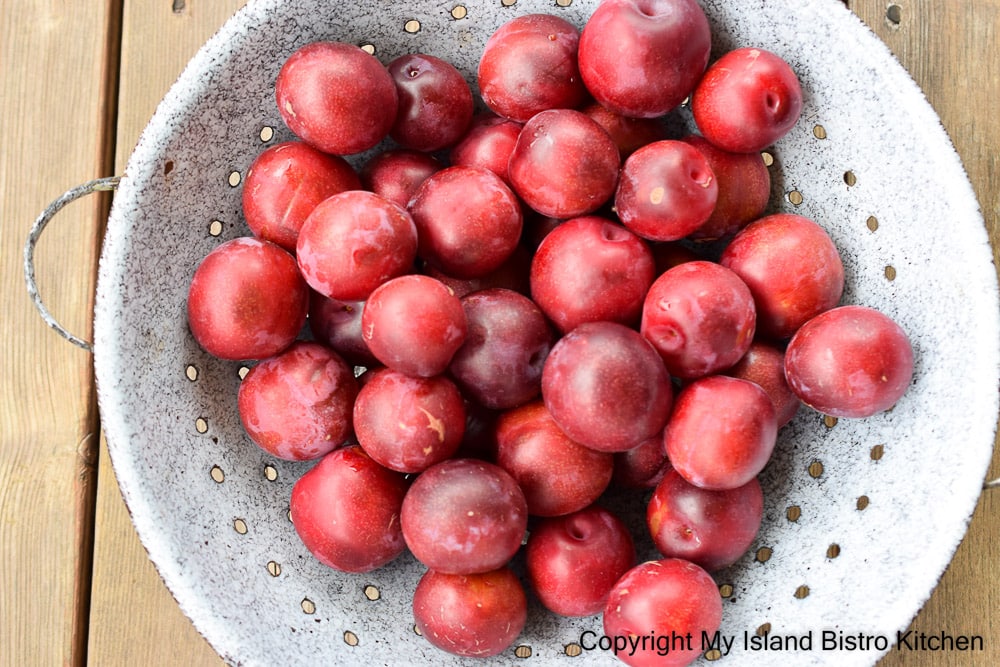 A blue enamel colander is filled with Vampire Red Plums