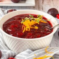 White bowl filled with homemade cranberry sauce garnished with orange slivers and a sprig of Rosemary