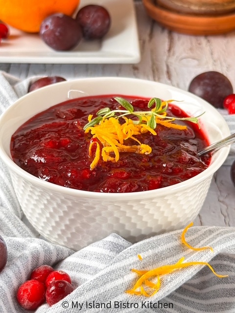 White bowl filled with cranberry sauce garnished with orange slivers and a sprig of Rosemary